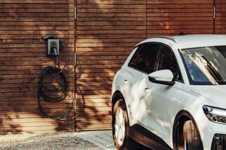 Weißes Elektro-SUV neben einer Ladestation an einer Holzwand